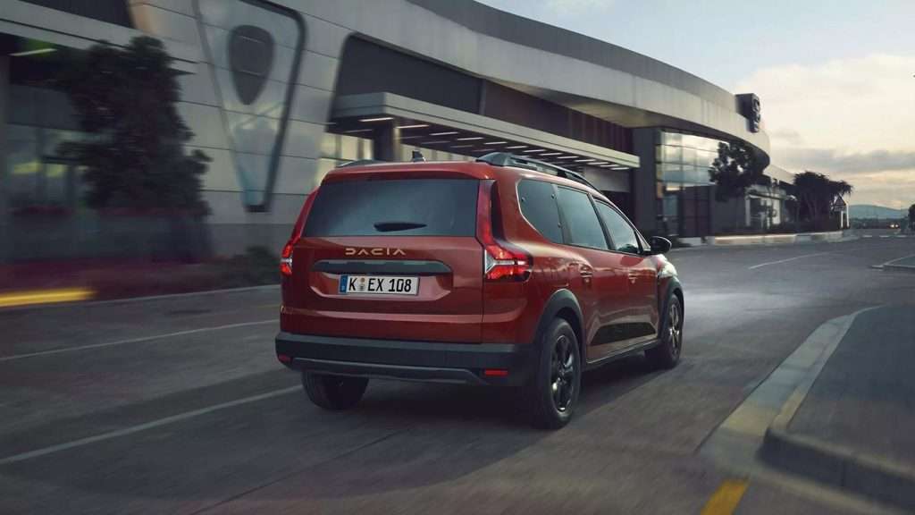 Dacia Jogger Rückansicht fahrend, vor einem großen modernen Stadtgebäude