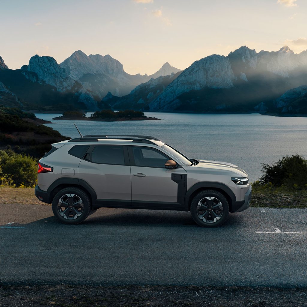 Dacia Duster in der Seitenansicht auf einer Straße vor Gebirgssee